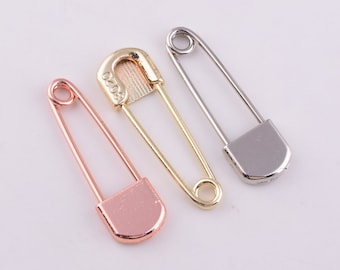Könnte beinhalten: Drei Sicherheitsnadeln in verschiedenen Farben: Gold, Silber und Roségold. Die Nadeln sind alle geschlossen und haben ein schlichtes Design.