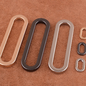 May include: Three oval-shaped metal rings in gold, black, and silver. There are three smaller rings in gold, black, and silver.