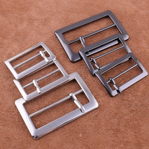 May include: Four silver belt buckles of different sizes. The buckles are rectangular with a smooth, polished finish.