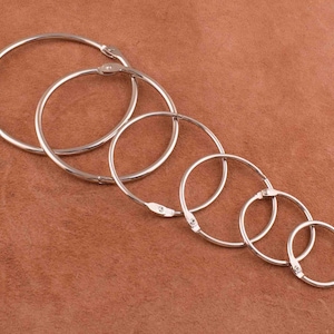 May include: A set of six silver metal binder rings of varying sizes. The rings are arranged in order of size, with the largest ring at the top and the smallest ring at the bottom.