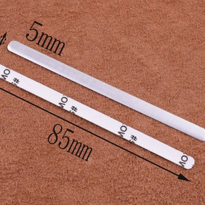 May include: Two silver metal strips, one measuring 5 mm wide and 85 mm long, on a brown textured surface.