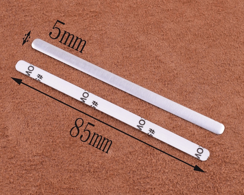May include: Two silver metal strips, one measuring 5 mm wide and 85 mm long, on a brown textured surface.
