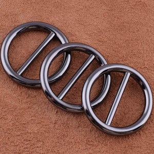 May include: Three black metal rings with a center bar. The rings are smooth and shiny.