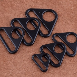 May include: A set of six black triangle-shaped metal slider buckles of varying sizes. The buckles have a smooth, polished finish.