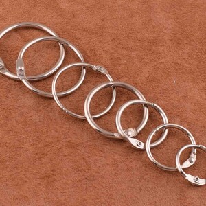 May include: A set of seven silver metal binder rings of varying sizes. The rings are arranged in order of size, with the largest ring at the top and the smallest ring at the bottom.