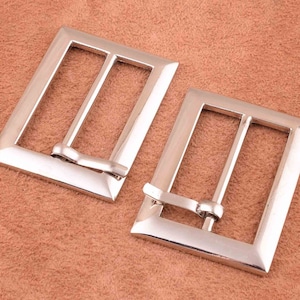 May include: Two silver metal belt buckles with a rectangular shape and a smooth finish.