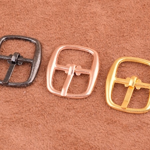 May include: Three metal belt buckles in different finishes: silver, rose gold, and gold. The buckles are square shaped with a smooth finish.