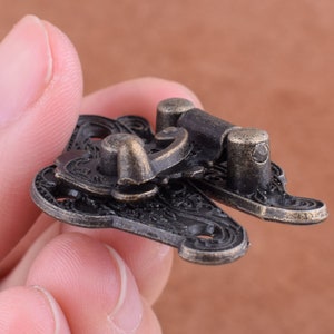May include: Antique-style brass latch with intricate floral designs. The latch has a hinged mechanism and a decorative knob.
