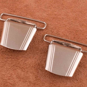 May include: Two silver metal clasps with a rectangular shape and a slightly curved top. The clasps have a smooth, shiny finish.