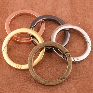 May include: Four metal key rings in different colors: gold, silver, bronze, and black. The rings are all open and have a spring-loaded clasp.