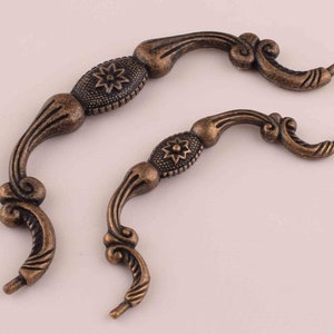 May include: Two antique-style cabinet pulls with ornate designs. The pulls are made of metal and have a dark bronze finish.