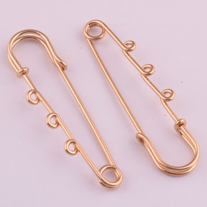 May include: Two gold safety pins with decorative loops. The pins are about 2 inches long.