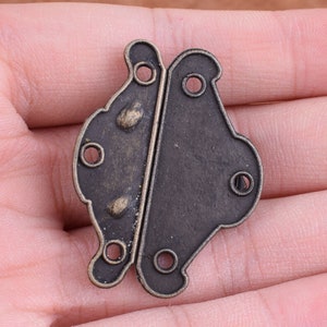 May include: Antique brass butterfly hinge with a decorative design. The hinge is closed and has a dark brown finish.