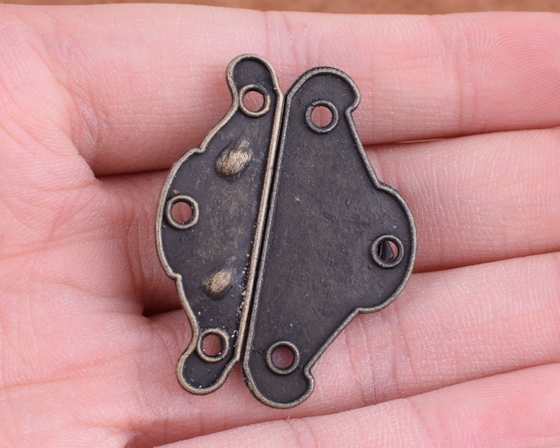 May include: Antique brass butterfly hinge with a decorative design. The hinge is closed and has a dark brown finish.