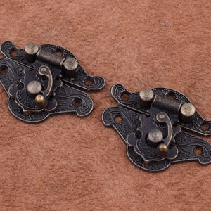 May include: Two antique-style metal clasps with ornate floral designs. Each clasp has a hinged latch and a decorative knob.