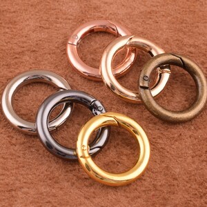May include: Five different metal key rings in various colors, including gold, silver, and bronze. The key rings are all closed and have a smooth finish.