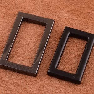 May include: Two metal rectangular frames, one is black and the other is a darker gray, both have a smooth finish.