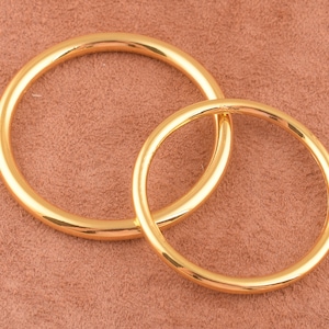 May include: Two gold-colored metal rings, one larger than the other, are stacked on top of each other. The rings are smooth and shiny.