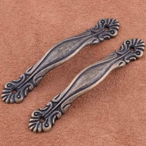 Peut inclure: Deux poignées de tiroir en métal ornées avec une finition vieillie. Les poignées ont un design décoratif avec un motif floral.