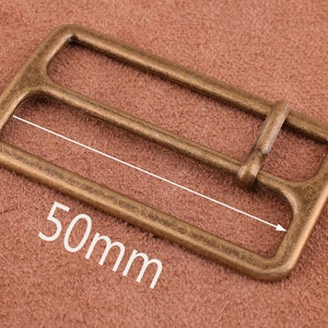 Può includere: Una fibbia in metallo color oro, di forma rettangolare, con due fessure per una cintura. La fibbia misura 50 mm di lunghezza.
