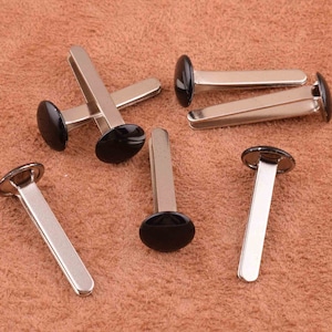 Könnte beinhalten: Ein Satz von zehn silbernen Metallösen mit schwarzen Kunststoffkappen. Die Ösen sind für die Verwendung in Lederbastelprojekten konzipiert.