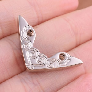 May include: Silver metal corner protector with a decorative swirl design.