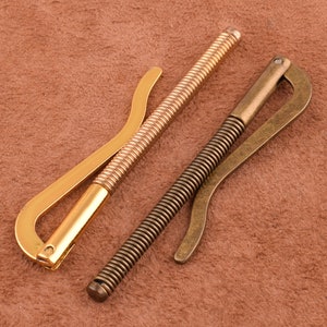 以下が含まれることがあります： ばね仕掛けの金色の金属製マネークリップが2つ。1つはシンプルなデザイン、もう1つは湾曲した形をしています。