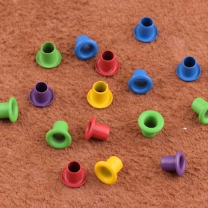 May include: Assortment of colorful metal eyelets in various sizes. The eyelets are arranged on a brown surface.