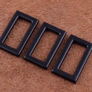May include: Three black metal rectangular frame shapes with rounded corners. The frames are different sizes and are arranged in a row.