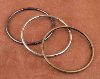 May include: Three metal rings in different sizes and finishes: a silver ring, a gold ring, and a black ring. The rings are stacked on top of each other.