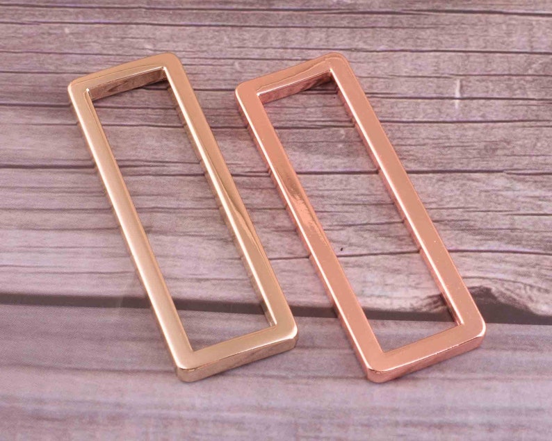 May include: Two rose gold metal rectangular frames. The frames are open on all sides and have a smooth, polished finish.