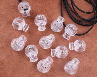 May include: A collection of clear plastic toggle stoppers with a metal spring inside. The stoppers are round and have a small hole in the top.