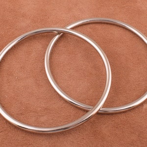 May include: Two silver metal rings, one slightly larger than the other, are interlocked and lying on a brown suede surface.