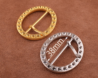May include: Two metal belt buckles, one gold and one silver. The gold buckle is 38 mm in diameter and has a round shape with a decorative pattern of small circles. The silver buckle is also round and has a similar decorative pattern.