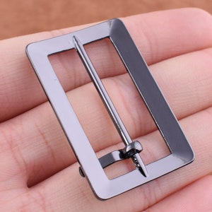 May include: A black metal belt buckle with a rectangular shape and a single, straight pin.