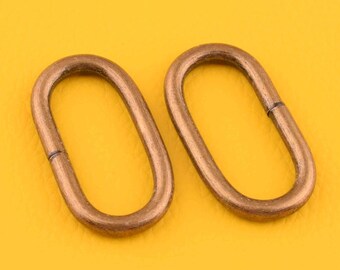 May include: Two oval-shaped metal rings in a brass finish. The rings are lying on a yellow surface.