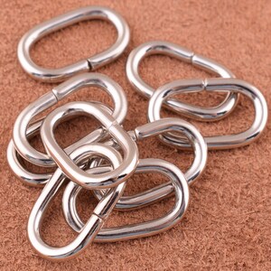 May include: A close-up of a group of silver metal rings, likely for attaching to leather goods. The rings are oval-shaped and have a smooth, polished finish.