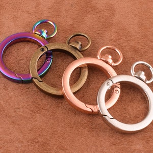 May include: Three metal key rings with a swivel clasp. The key rings are in different colors: iridescent, antique brass, and silver.