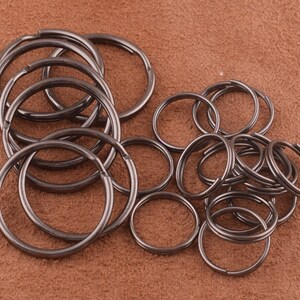 May include: A pile of black metal key rings. The key rings are all different sizes and are arranged in a random pattern.