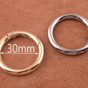 May include: Two metal key rings, one gold and one silver, with a 30mm diameter. The gold key ring is on the left and the silver key ring is on the right.