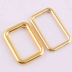May include: Two gold-colored metal rectangular rings. The rings are open on one side and have a smooth, polished finish.