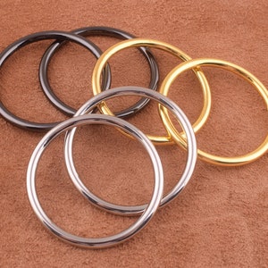 May include: Five metal rings of different sizes and colors. The rings are made of gold, silver, and black metal. They are arranged in a circle, with the largest ring on the outside and the smallest ring on the inside.