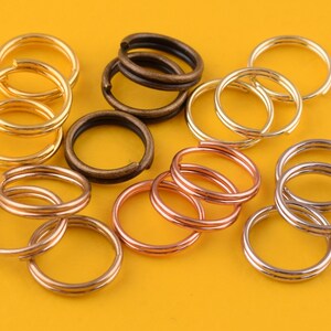 Könnte beinhalten: Sortiment an Schlüsselringen in Gold, Silber, Bronze und Kupfer. Die Schlüsselringe sind gestapelt und auf einer gelben Oberfläche angeordnet.