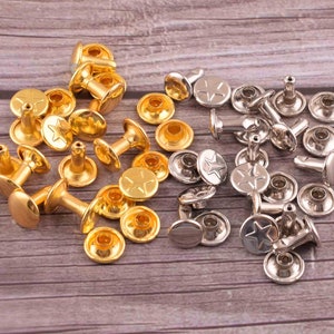 Puede incluir: Una colección de remaches de metal dorado y plateado con un diseño de estrella. Los remaches se utilizan para sujetar tela, cuero u otros materiales.