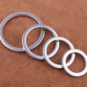 May include: Four silver key rings of different sizes, arranged in a circle on a brown surface.