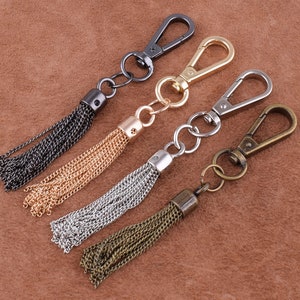 May include: Four keychains with different colored tassels. The keychains are made of metal and have a hook closure. The tassels are made of chain links and are available in black, gold, silver, and bronze.