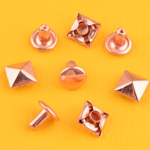 May include: Assortment of eight rose gold metal rivets, including pyramid, round, and square shapes.