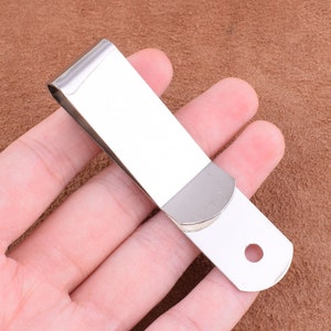 May include: Silver metal money clip with a rounded edge and a hole in the center. The clip is designed to hold bills and cash.