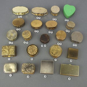 Op de afbeelding: Een assortiment vintage pillendoosjes in verschillende vormen en maten. De collectie omvat ronde, ovale en vierkante doosjes, sommige met sierlijke gouden details en andere met een eenvoudige, metalen afwerking. Er is ook een groen hartvormig doosje aanwezig.