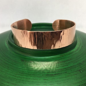 May include: A hammered copper cuff bracelet with a textured finish. The bracelet is a warm copper colour and has a simple, elegant design.